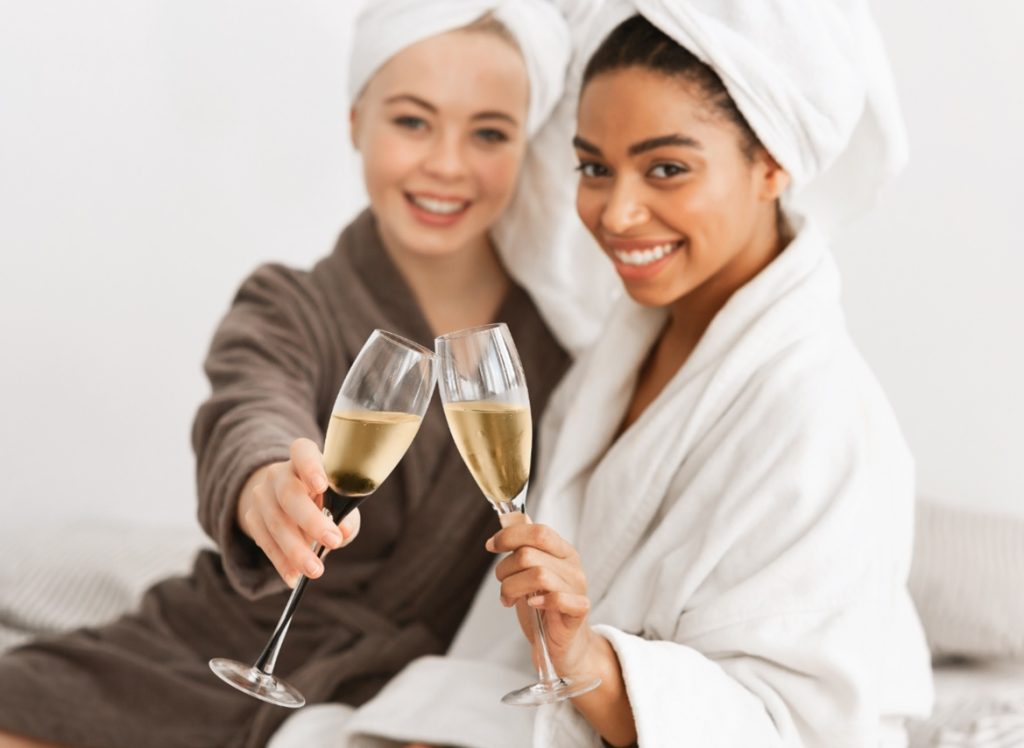 mujer de tez blanca y mujer de tez morena en spa brindando en copas con champaña